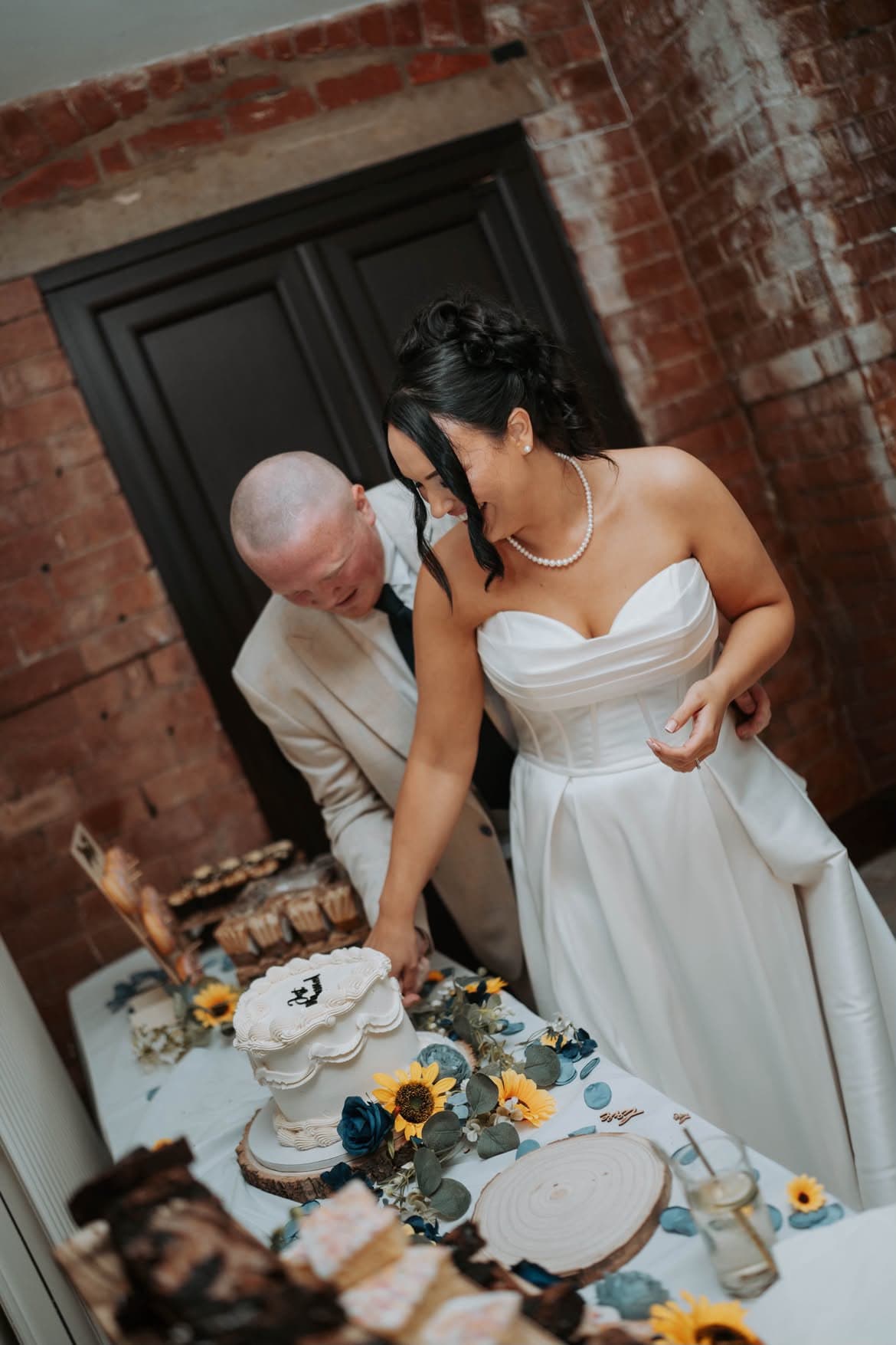 A couple cutting a wedding cake dressed with sunflowers