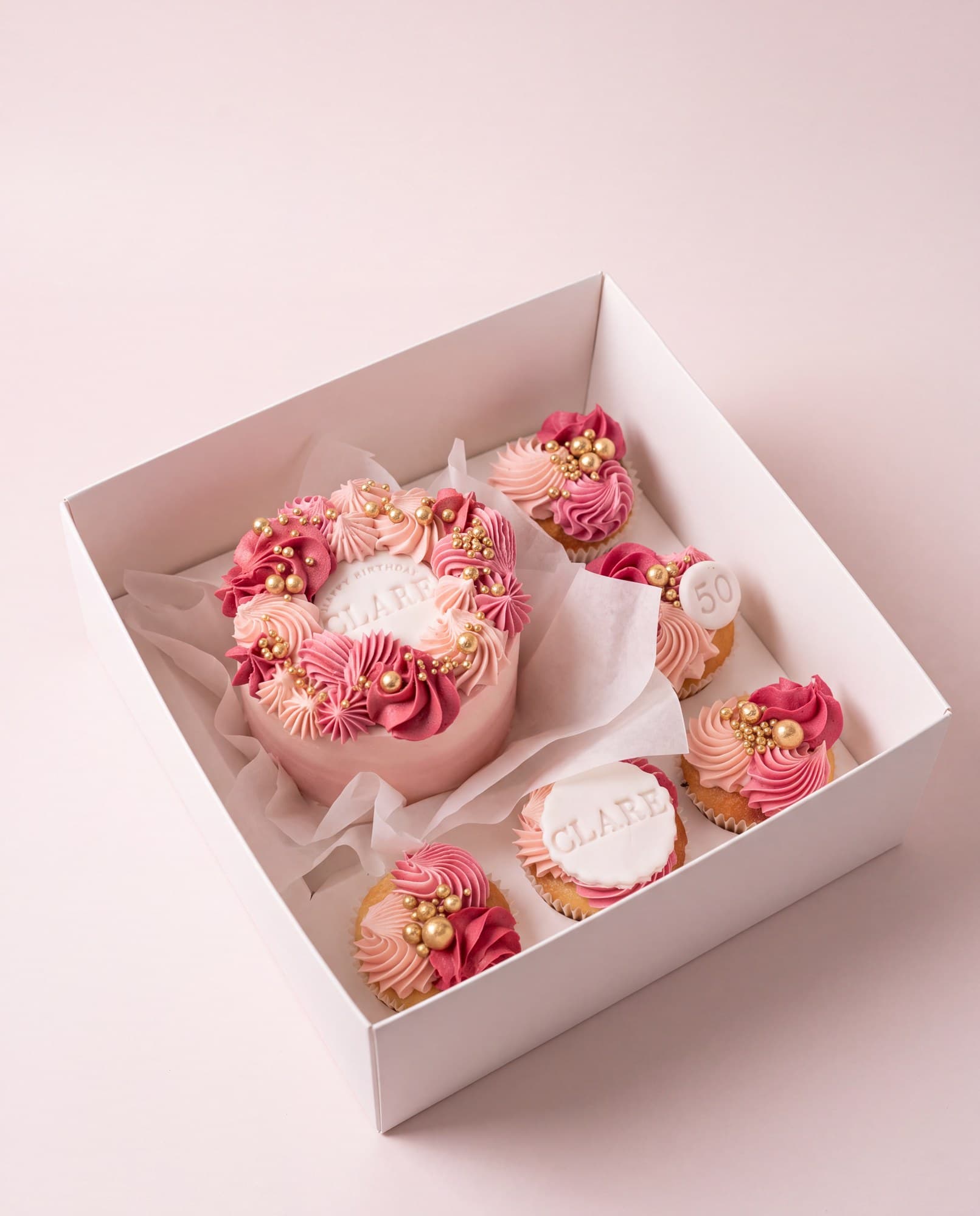 Bento box with a small pink cake and matching cupcakes